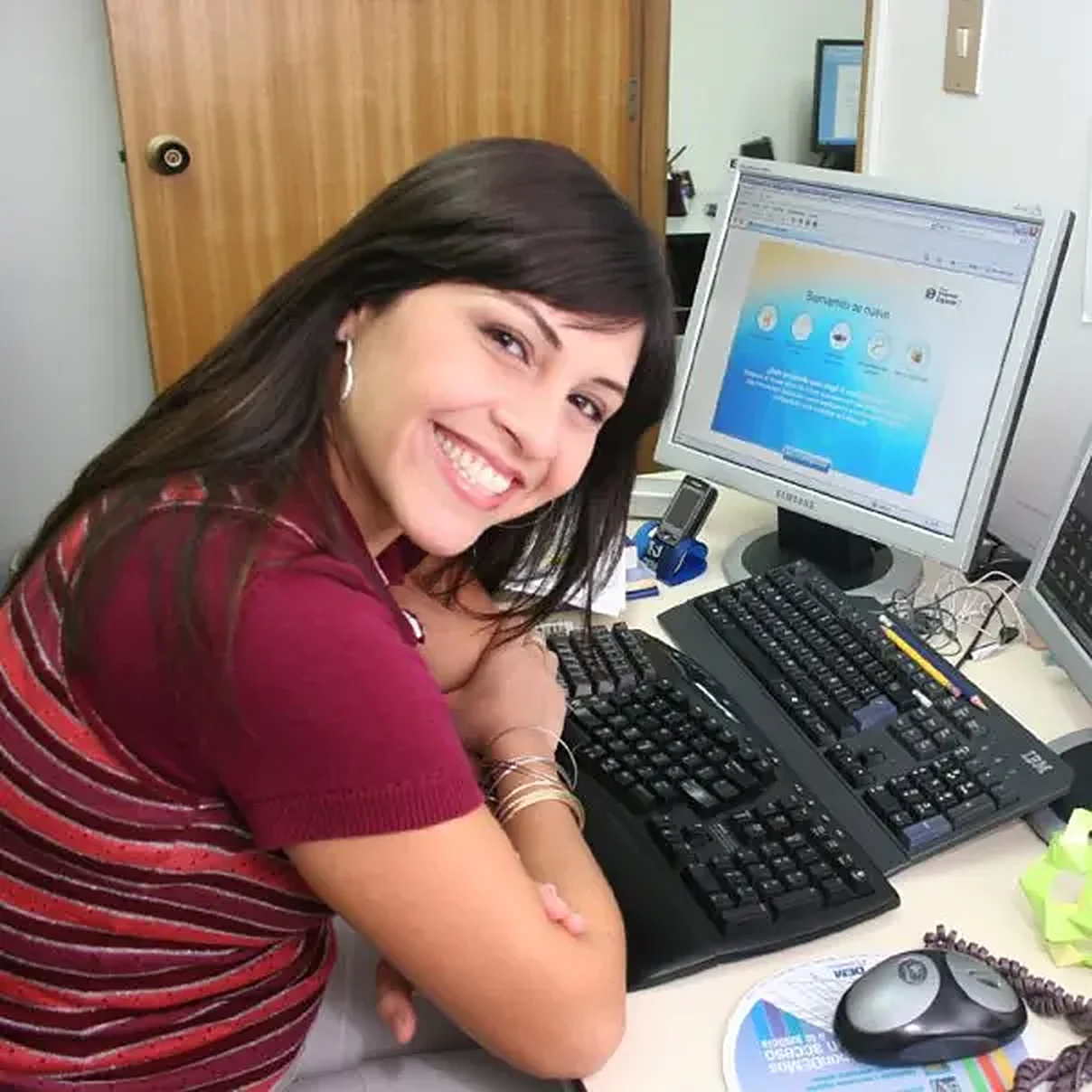 Photo of Emir Manrique in 2008, smiling at her desk next to a monitor showing the design of a web portal.